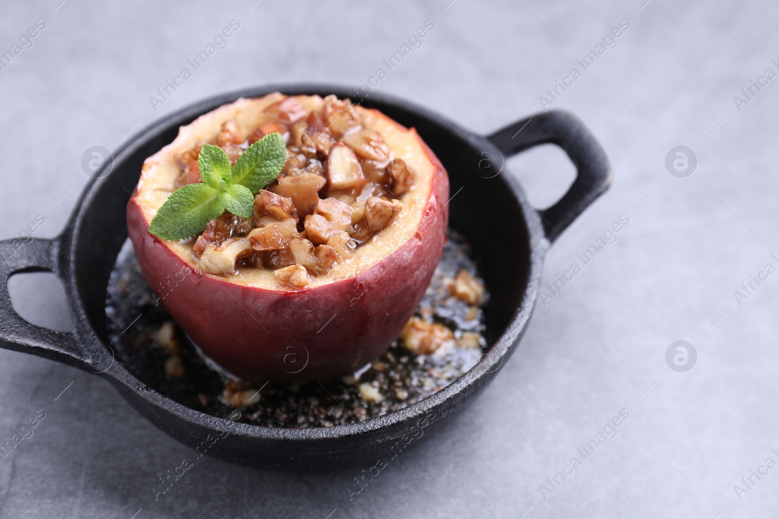 Photo of Tasty baked apple with nuts, honey and mint in baking dish on gray table, closeup