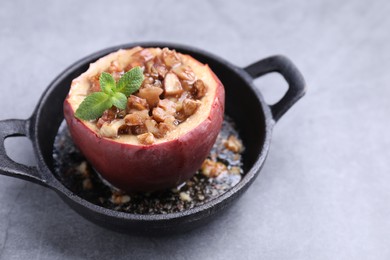 Tasty baked apple with nuts, honey and mint in baking dish on gray table, closeup