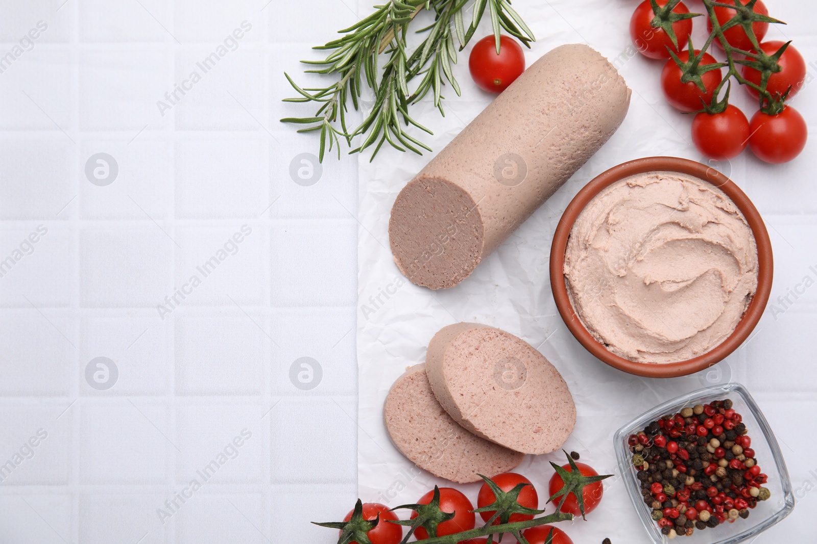 Photo of Delicious liver sausage, paste and other products on white tiled table, flat lay. Space for text