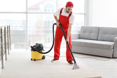 Male worker cleaning carpet with vacuum in living room