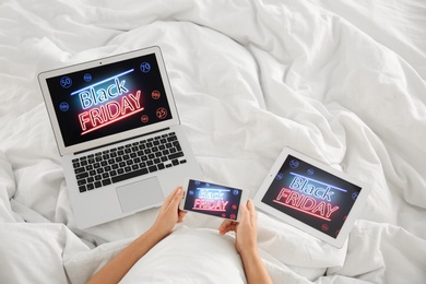 Photo of Woman using tablet, mobile phone and laptop with Black Friday announcement while lying in bed, above view