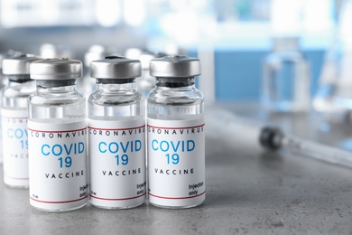 Photo of Glass vials with COVID-19 vaccine on grey table. Space for text