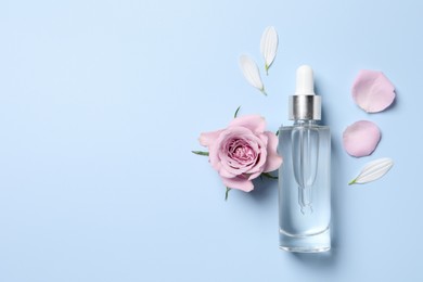 Bottle of cosmetic serum, beautiful flower and petals on light blue background, flat lay. Space for text