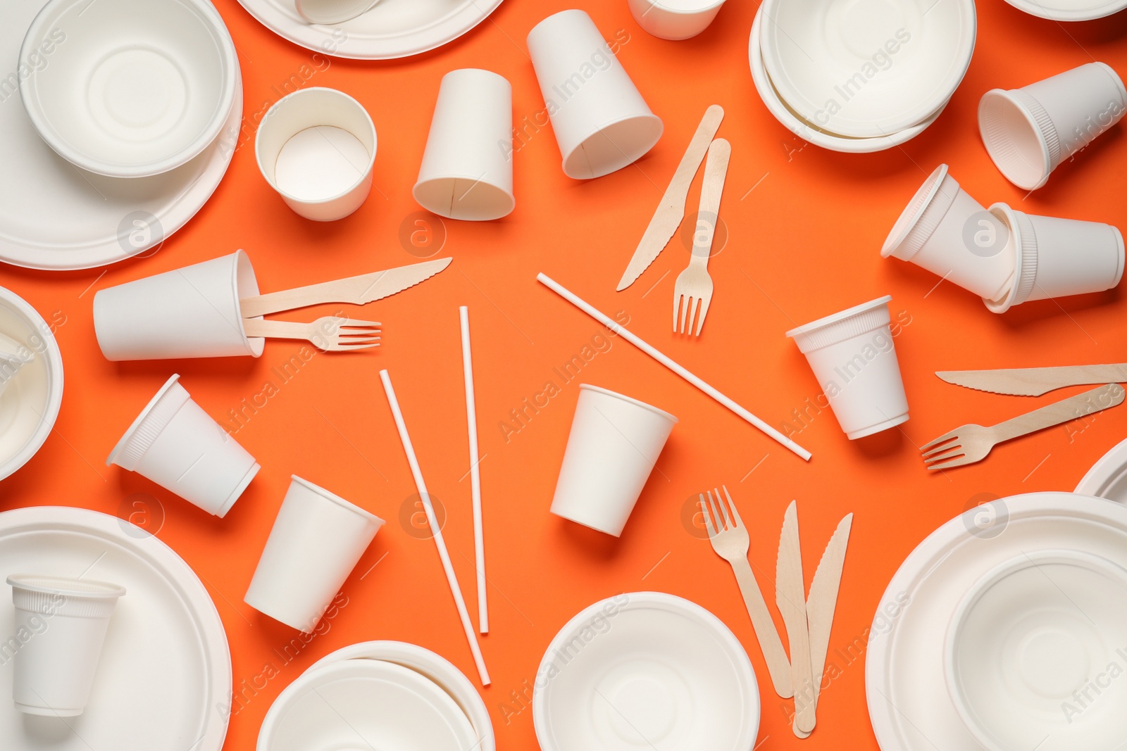 Photo of Disposable tableware on orange background, flat lay