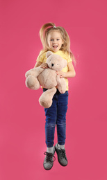 Photo of Little girl with teddy bear jumping on pink background