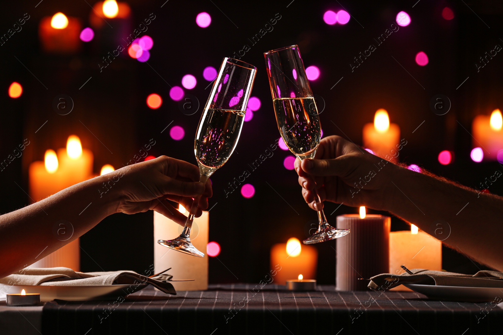 Photo of Young couple with glasses of champagne having romantic candlelight dinner at table, closeup