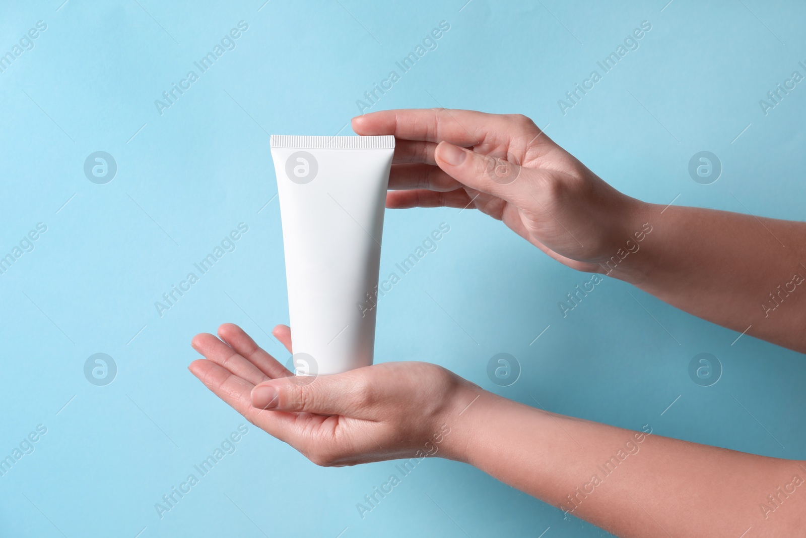 Photo of Woman with tube of hand cream on light blue background, closeup