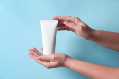 Woman with tube of hand cream on light blue background, closeup