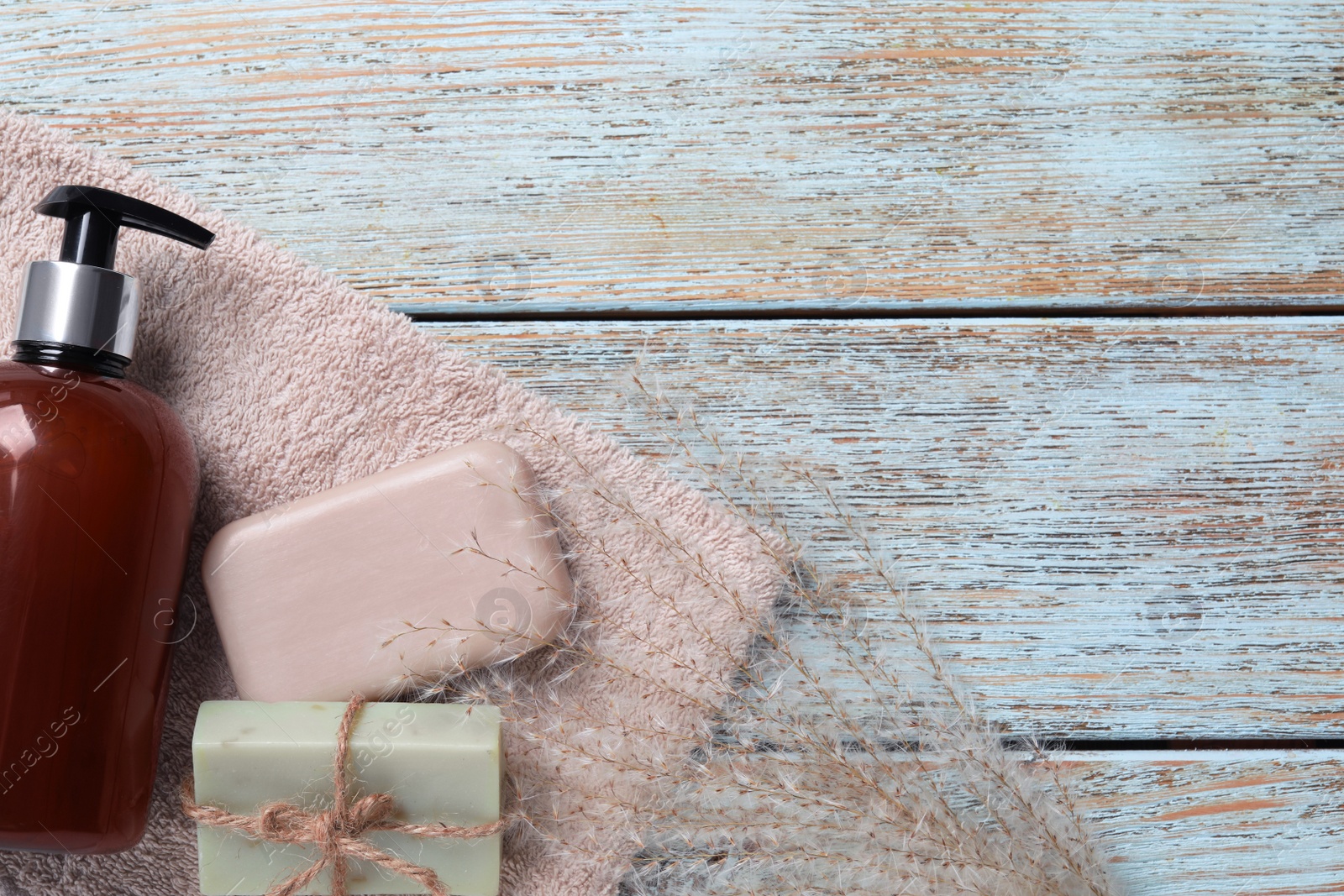 Photo of Soap bars, dispenser and terry towel on light blue wooden table, flat lay. Space for text