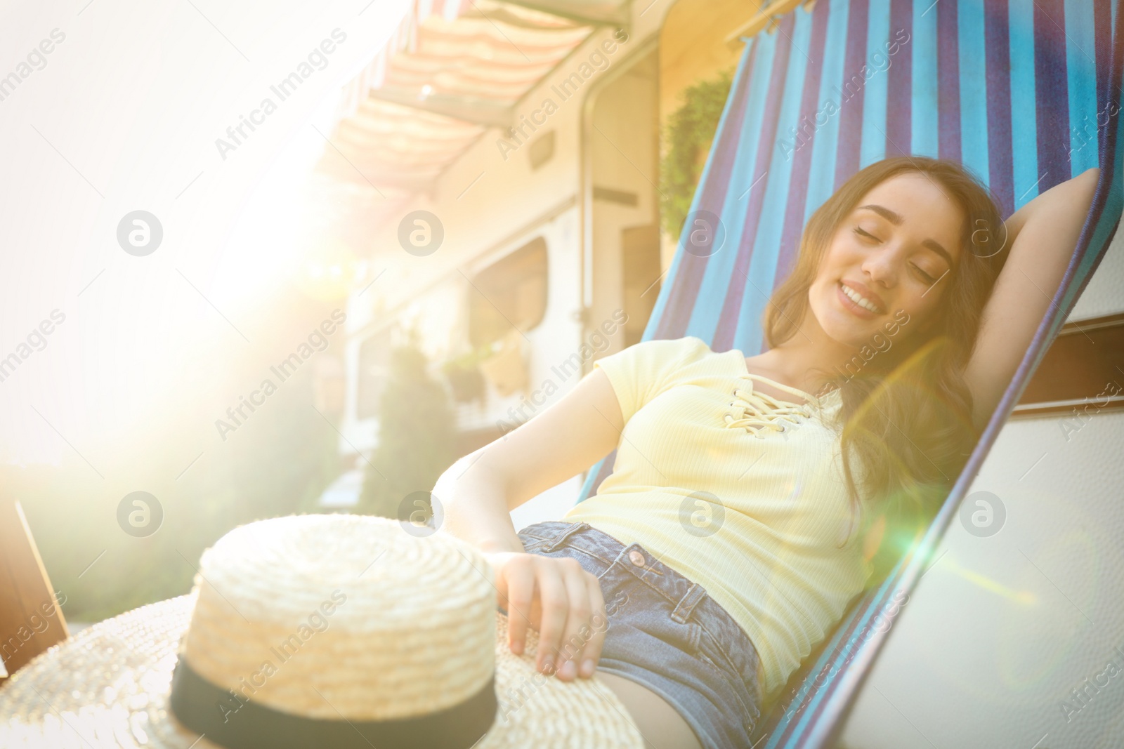 Photo of Young woman with hat resting in hammock near motorhome outdoors on sunny day