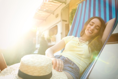 Photo of Young woman with hat resting in hammock near motorhome outdoors on sunny day