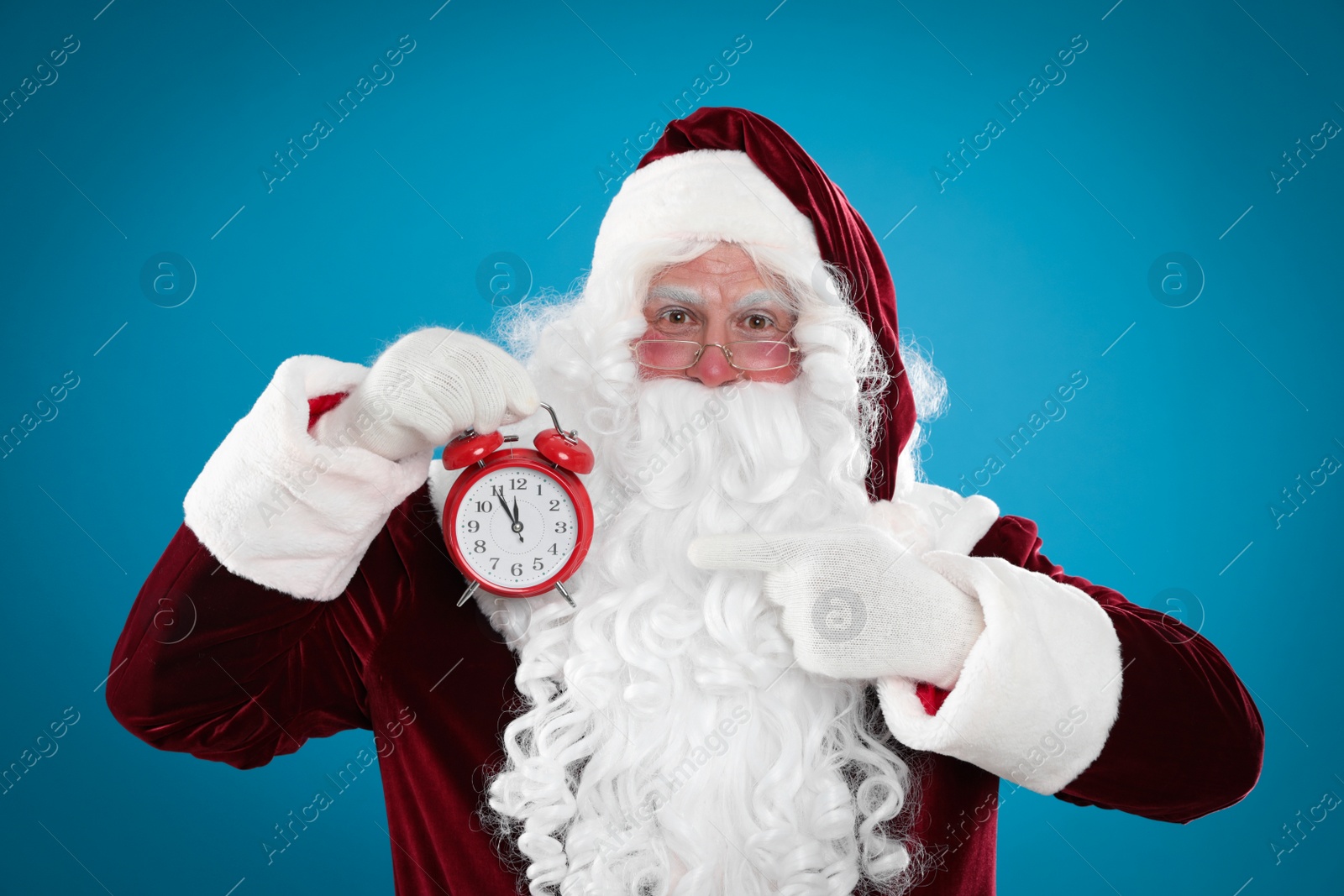 Photo of Santa Claus holding alarm clock on blue background. Christmas countdown