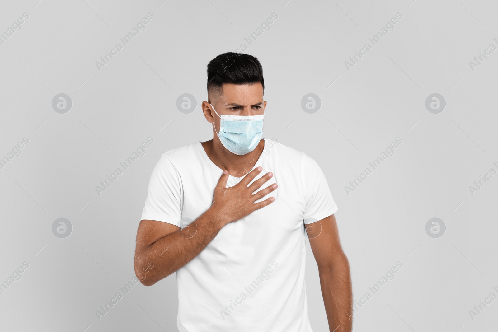 Photo of Man in medical mask suffering from pain during breathing on grey background