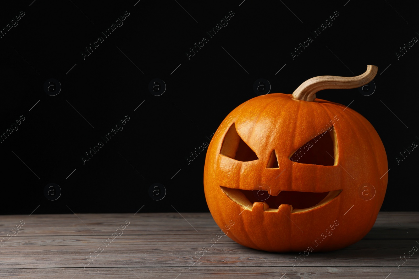 Photo of Scary jack o'lantern made of pumpkin on wooden table against black background, space for text. Halloween traditional decor