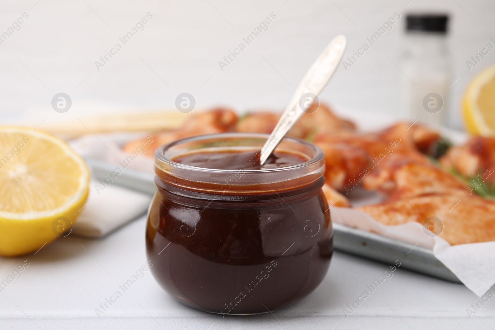 Photo of Fresh marinade with spoon in jar on light tiled table, closeup