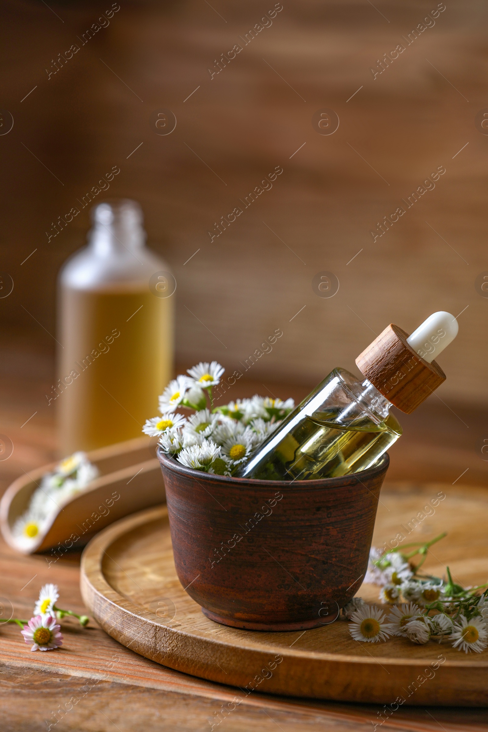 Photo of Bottle of chamomile essential oil and flowers on wooden table