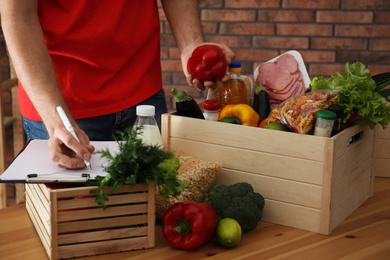Man with fresh products at table indoors, closeup. Food delivery service