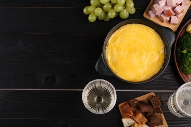 Photo of Fondue pot with melted cheese and different products on black wooden table, flat lay. Space for text