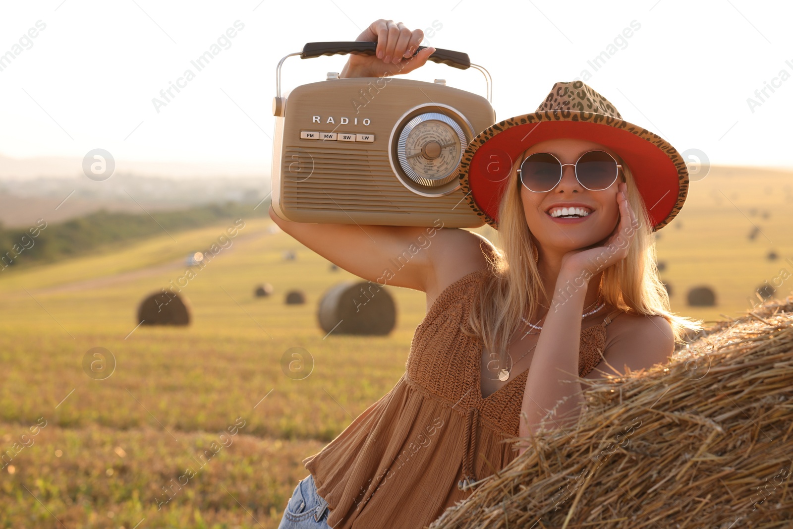 Photo of Happy hippie woman with radio receiver near hay bale in field, space for text