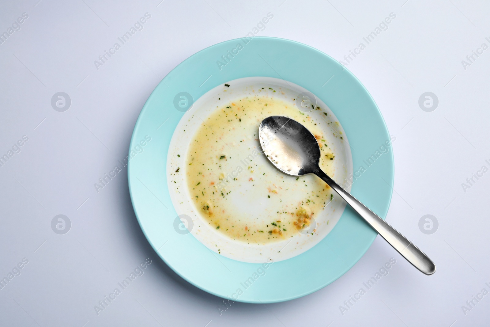 Photo of Dirty plate with leftovers and spoon on white background, top view