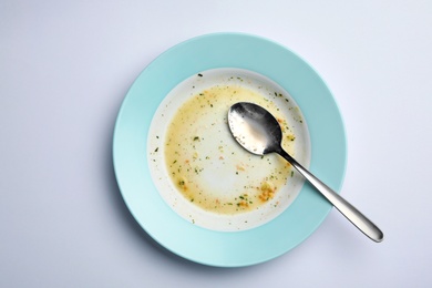 Photo of Dirty plate with leftovers and spoon on white background, top view