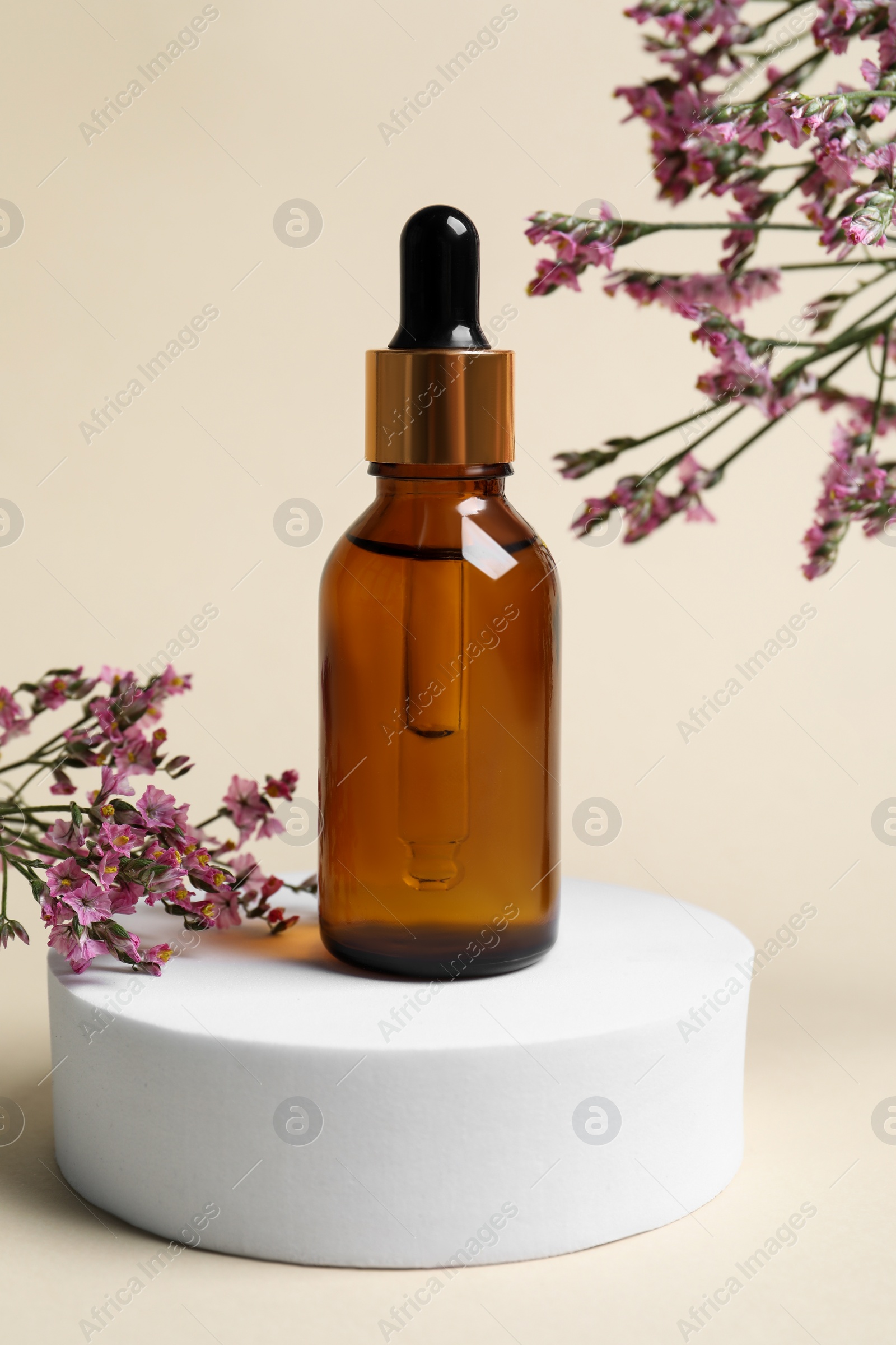 Photo of Bottle of cosmetic oil and flowers on beige background, closeup