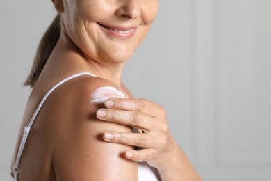 Photo of Happy woman applying body cream onto shoulder near white wall, closeup. Space for text