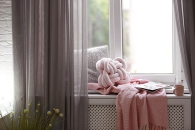 Photo of Cozy place with pillows and plaid on windowsill in room interior. Unusual cushion design