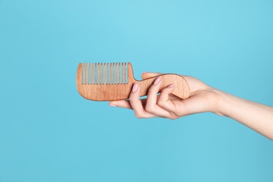 Photo of Woman holding wooden hair comb against blue background, closeup