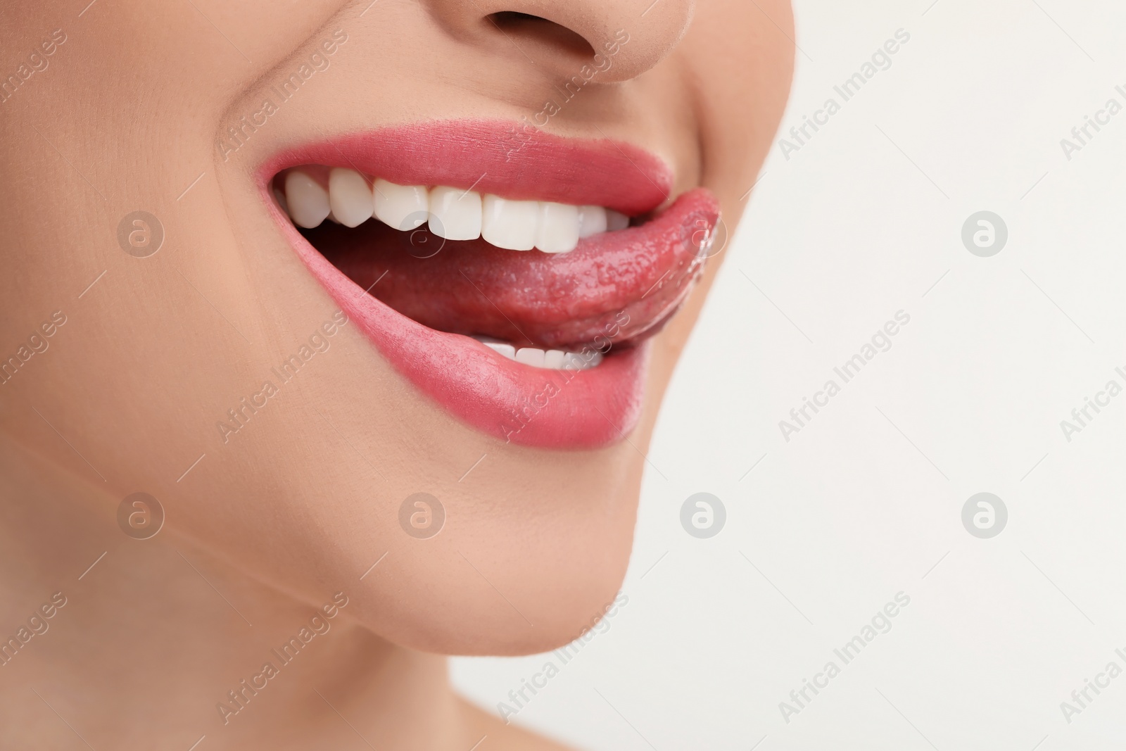 Photo of Young woman licking her teeth on white background, closeup
