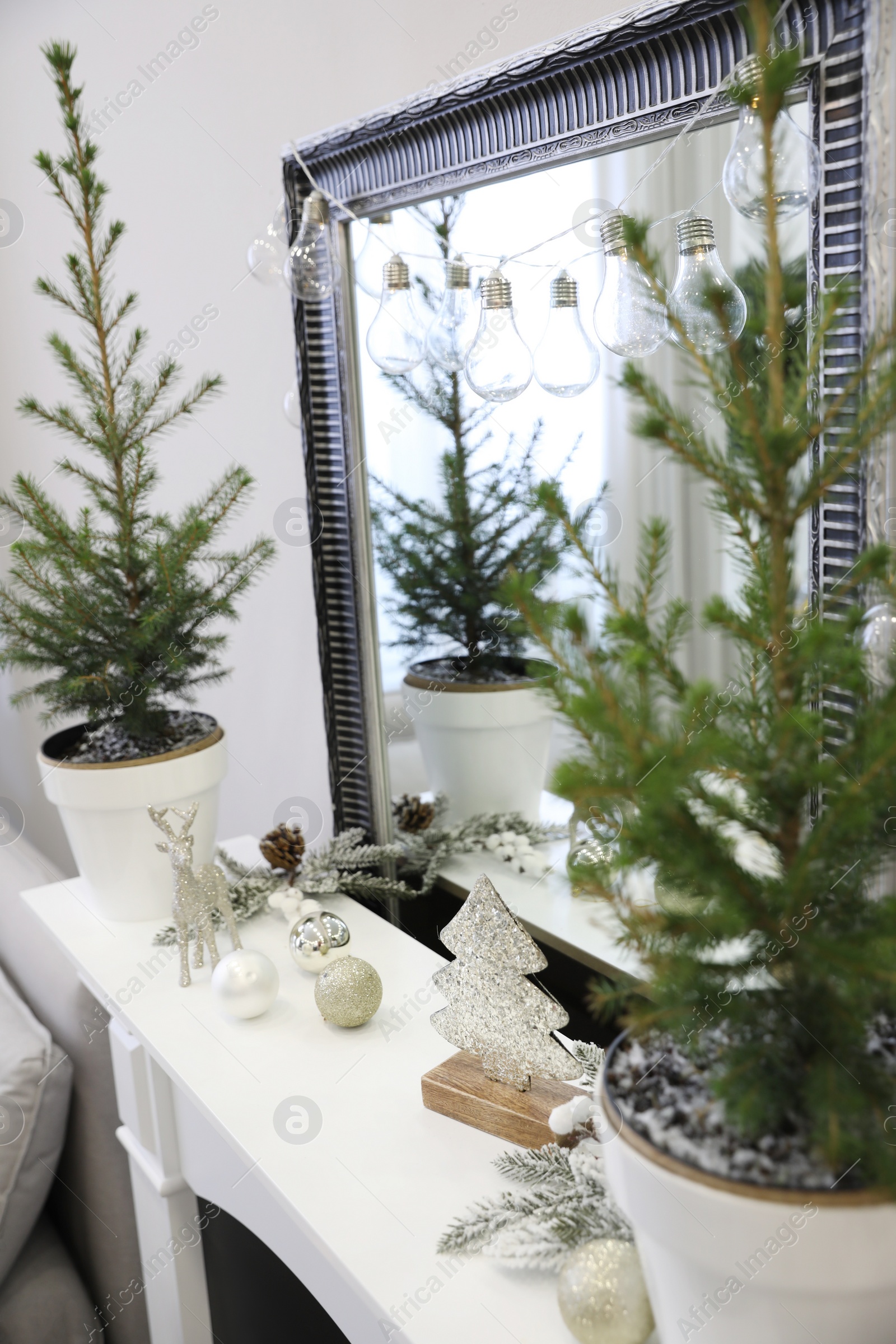 Photo of Little fir trees and Christmas decorations on mantelpiece in room. Stylish interior design