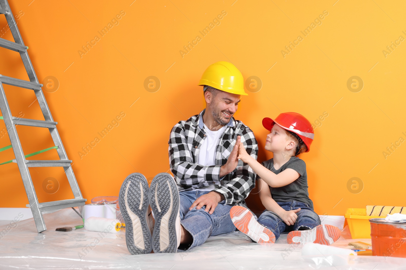 Photo of Father and son with repair tools near orange wall