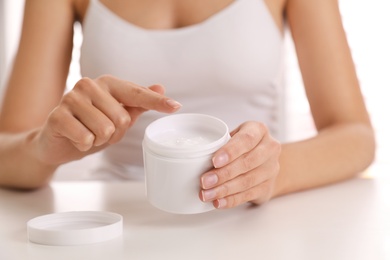 Photo of Woman with jar of moisturizing cream at white table, closeup