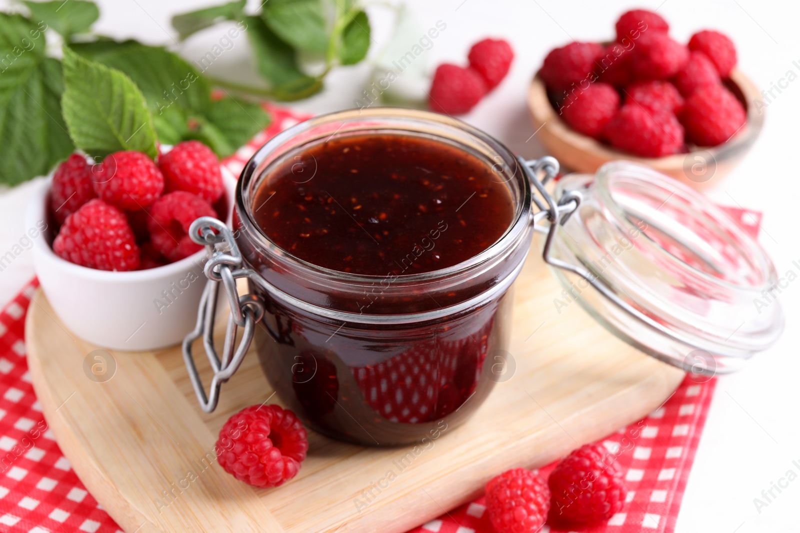 Photo of Jar of delicious raspberry jam and fresh berries on table, closeup