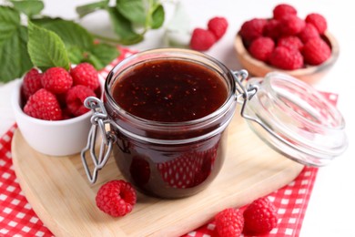 Photo of Jar of delicious raspberry jam and fresh berries on table, closeup