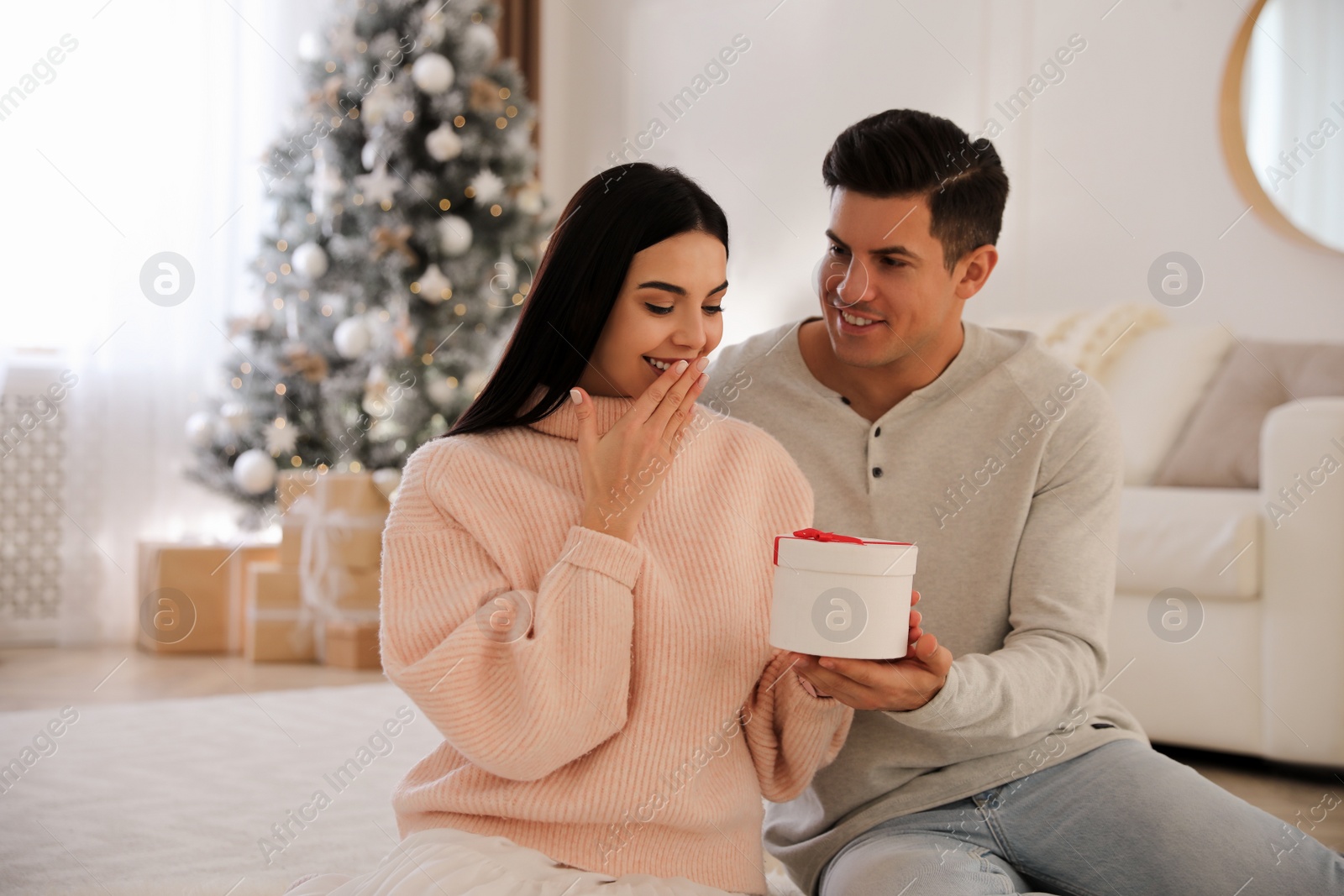 Photo of Boyfriend giving Christmas gift box to his girlfriend in living room