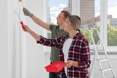 Photo of Happy couple painting wall in apartment during repair