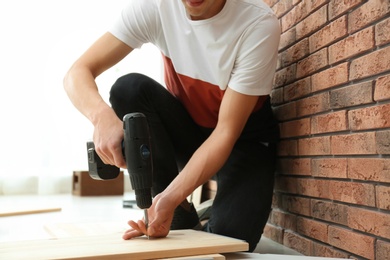 Photo of Man working with electric screwdriver near brick wall, closeup