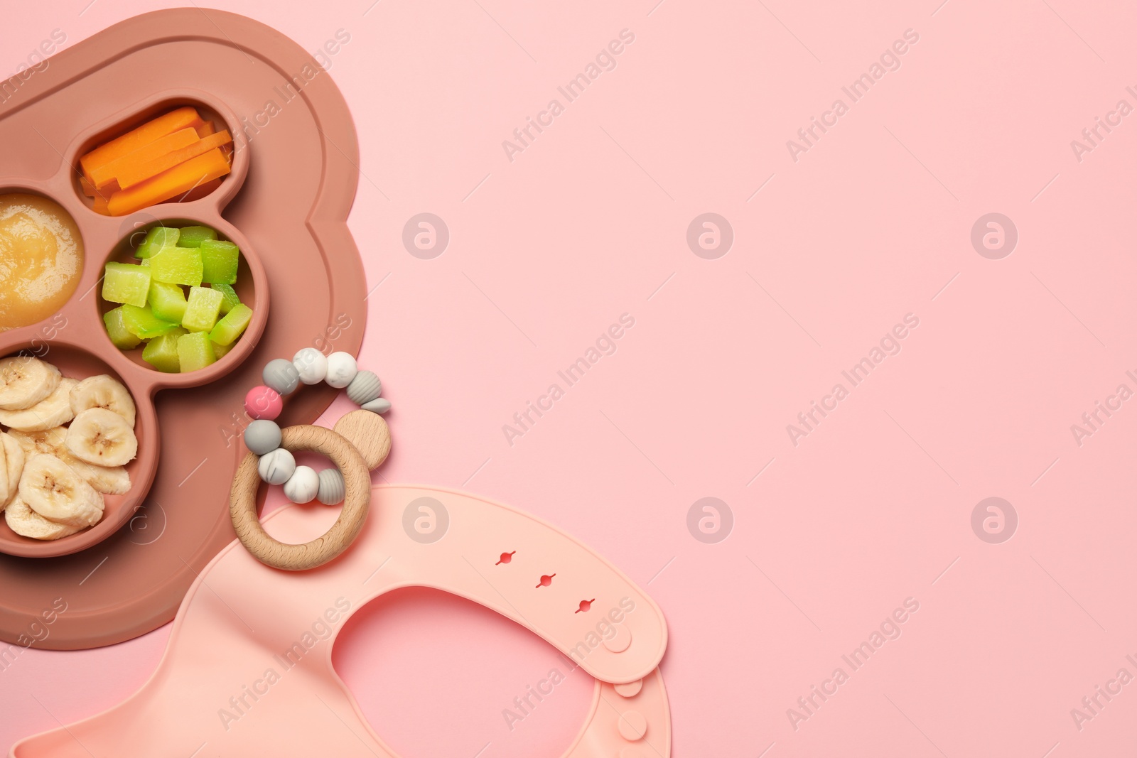 Photo of Section plate with healthy baby food, toy and bib on pink background, flat lay. Space for text