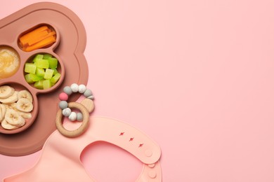 Photo of Section plate with healthy baby food, toy and bib on pink background, flat lay. Space for text