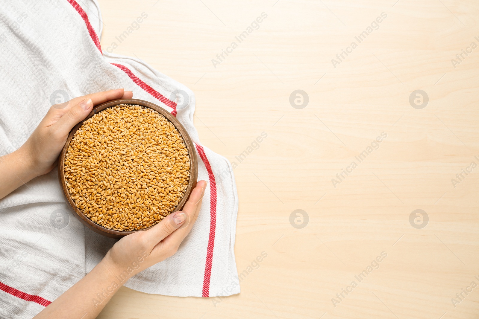 Photo of Woman holding bowl of wheat grains at white wooden table, top view. Space for text