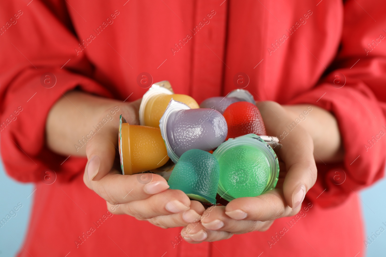 Photo of Woman holding many tasty bright jelly cups on light blue background, closeup