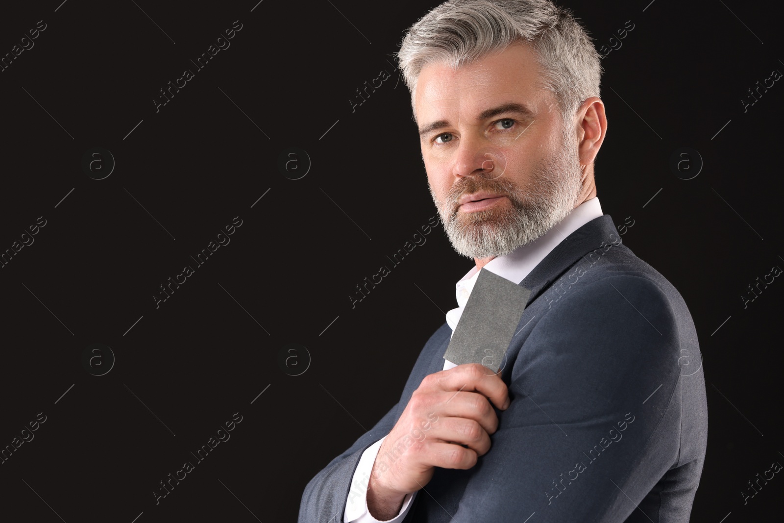 Photo of Handsome businessman holding blank business card on black background. Space for text