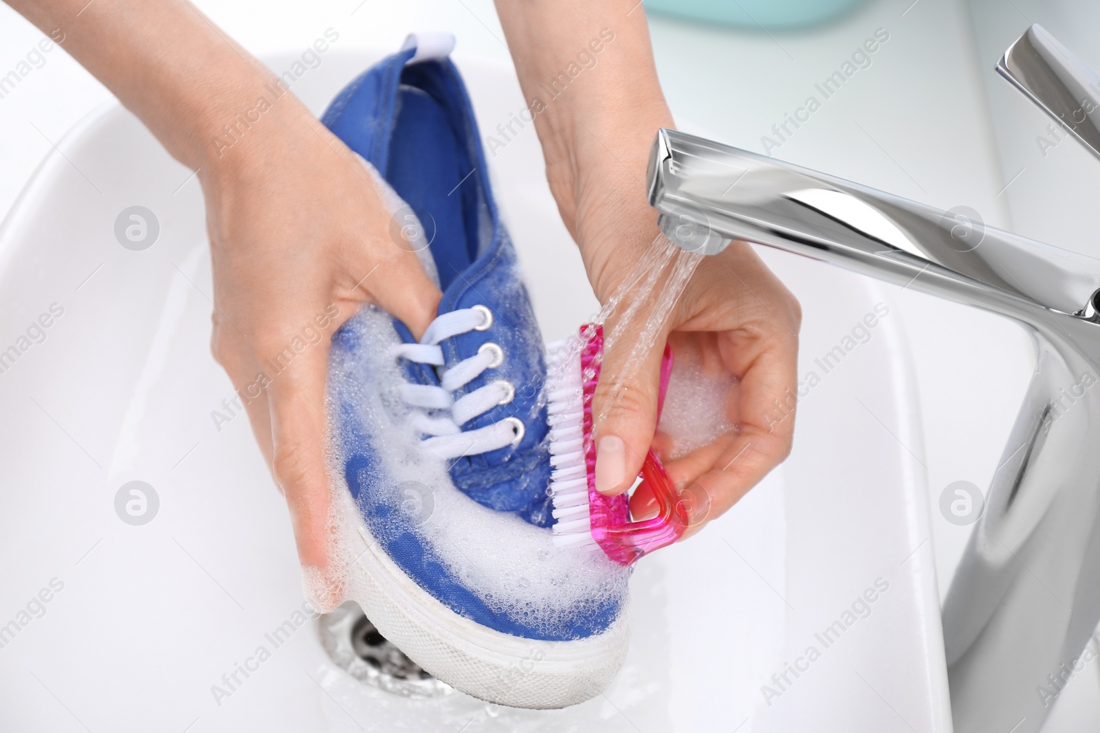 Photo of Woman washing shoe with brush under tap water in sink, closeup