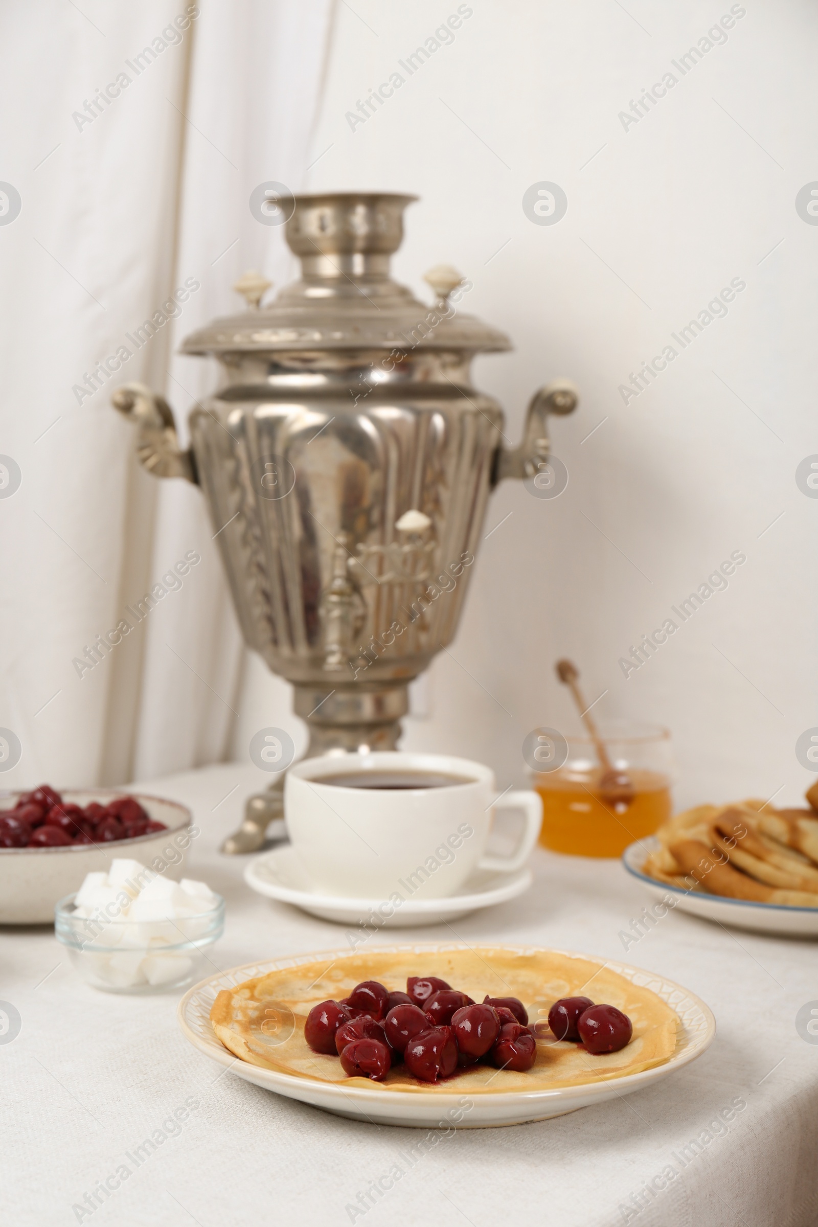 Photo of Vintage samovar, cup of hot drink and snacks served on table. Traditional Russian tea ceremony