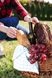 Woman taking bread from wicker basket outdoors, closeup. Picnic season
