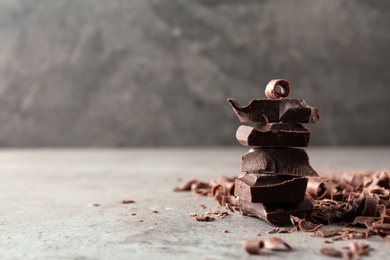 Photo of Curls and pieces of tasty chocolate on gray table. Space for text