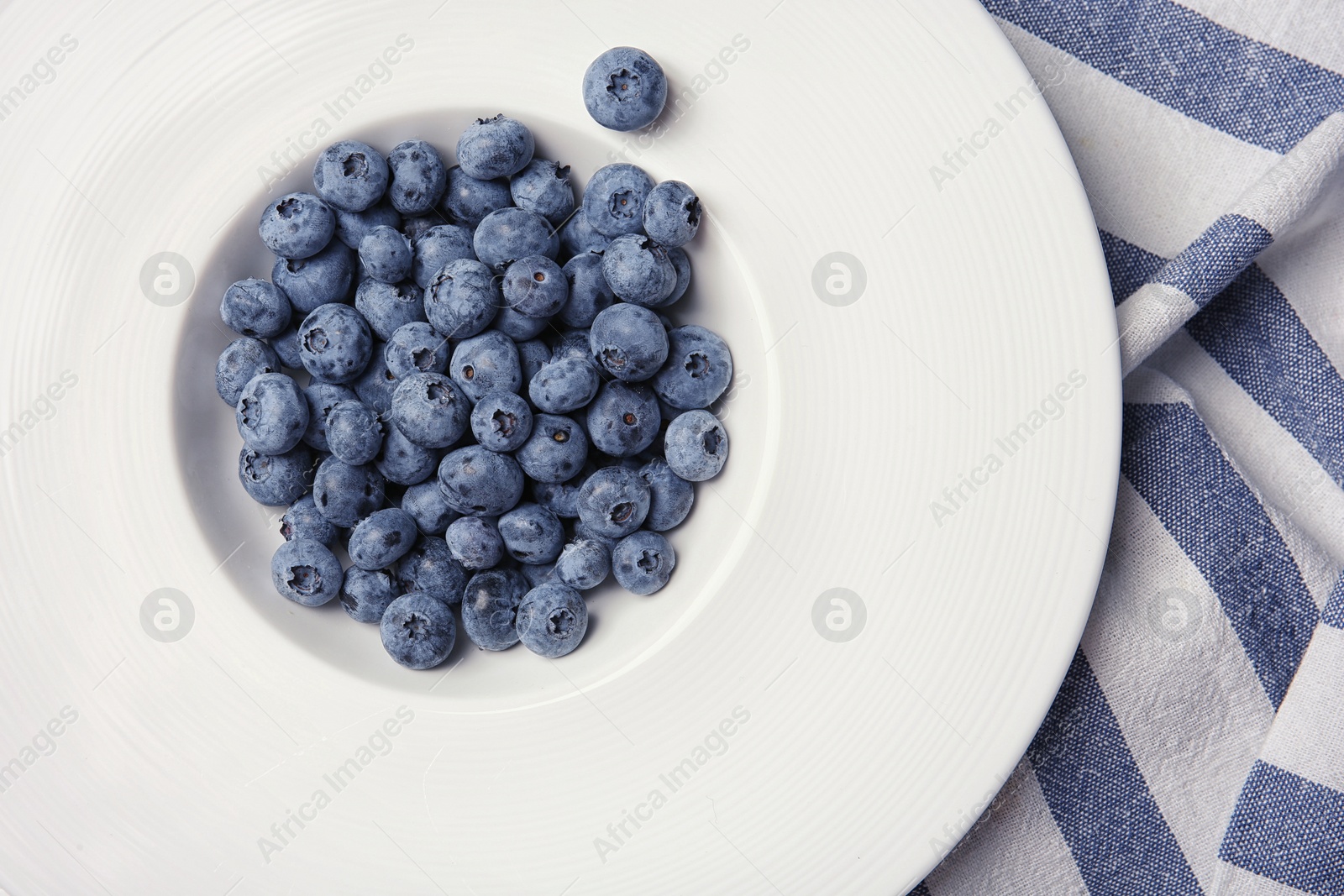 Photo of Fresh and juicy blueberries in white plate, top view