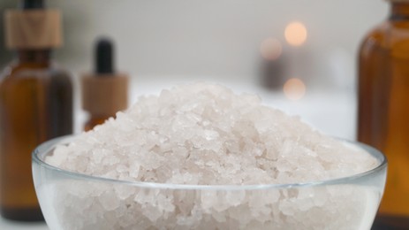 Photo of Glass bowl with bath salt and cosmetic products indoors, closeup