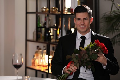 Photo of Happy man with roses waiting for his girlfriend in restaurant on Valentine's day